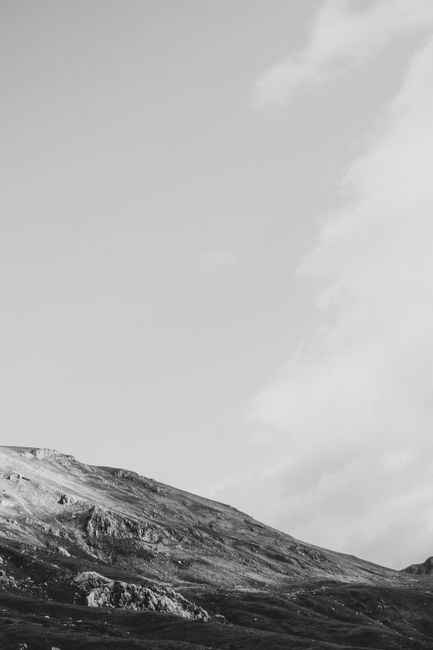 A serene grayscale landscape of a rocky mountain slope beneath a vast cloudy sky.