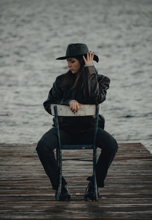 Woman Wearing a Cowboy Hat Sitting on a Chair on a Pier 