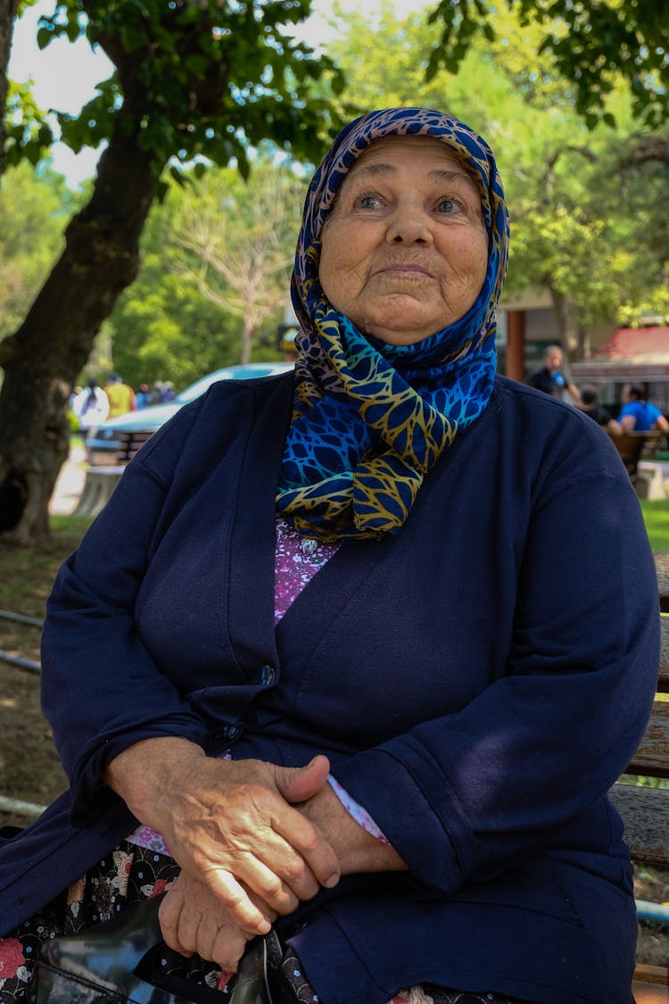 Elderly Woman In A Headscarf Sitting On A Bench In A Park 