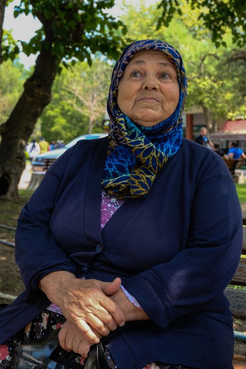 Free Elderly woman in headscarf sits on a bench in a serene park setting. Stock Photo