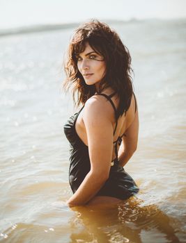 Stylish woman in a black swimsuit enjoying summer at the beach with a serene expression.
