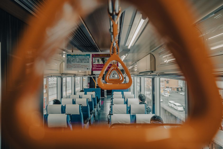 Interior view of a public train showing empty seats and handrails through a forward perspective.