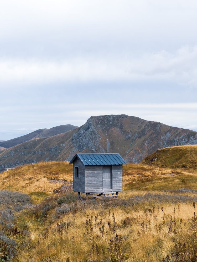 Small Shed In A Landscape With Dry Grass And Rocky Mountains