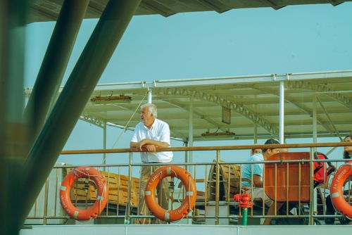 Free Elderly man enjoying a peaceful moment on a boat deck, surrounded by calm waters and sunny skies. Stock Photo