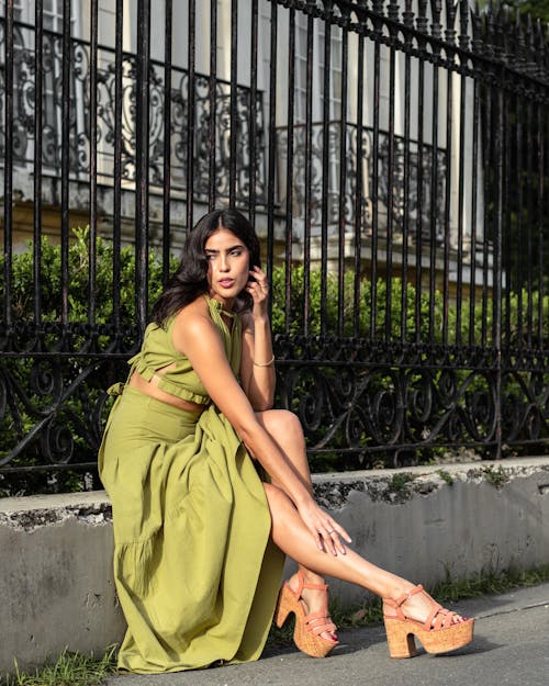 A Woman in Green Dress Sitting Beside the Metal Railings