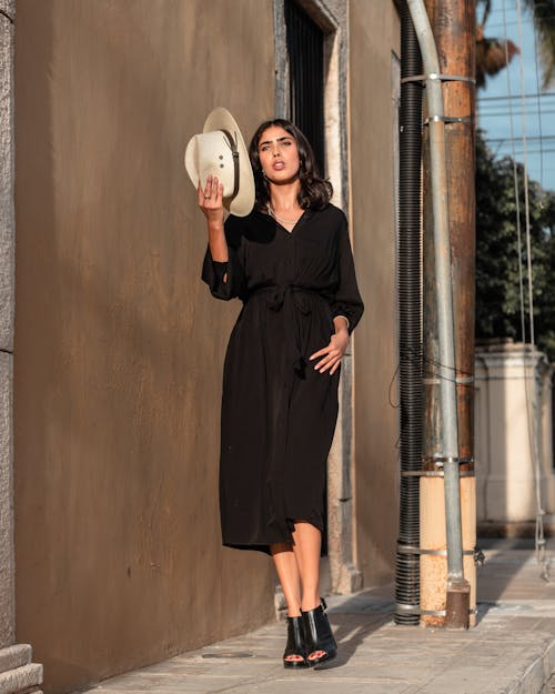 Woman in Black Dress Standing Beside Brown Wall