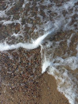 A serene close-up of a pebble beach with gentle waves lapping at the shore.