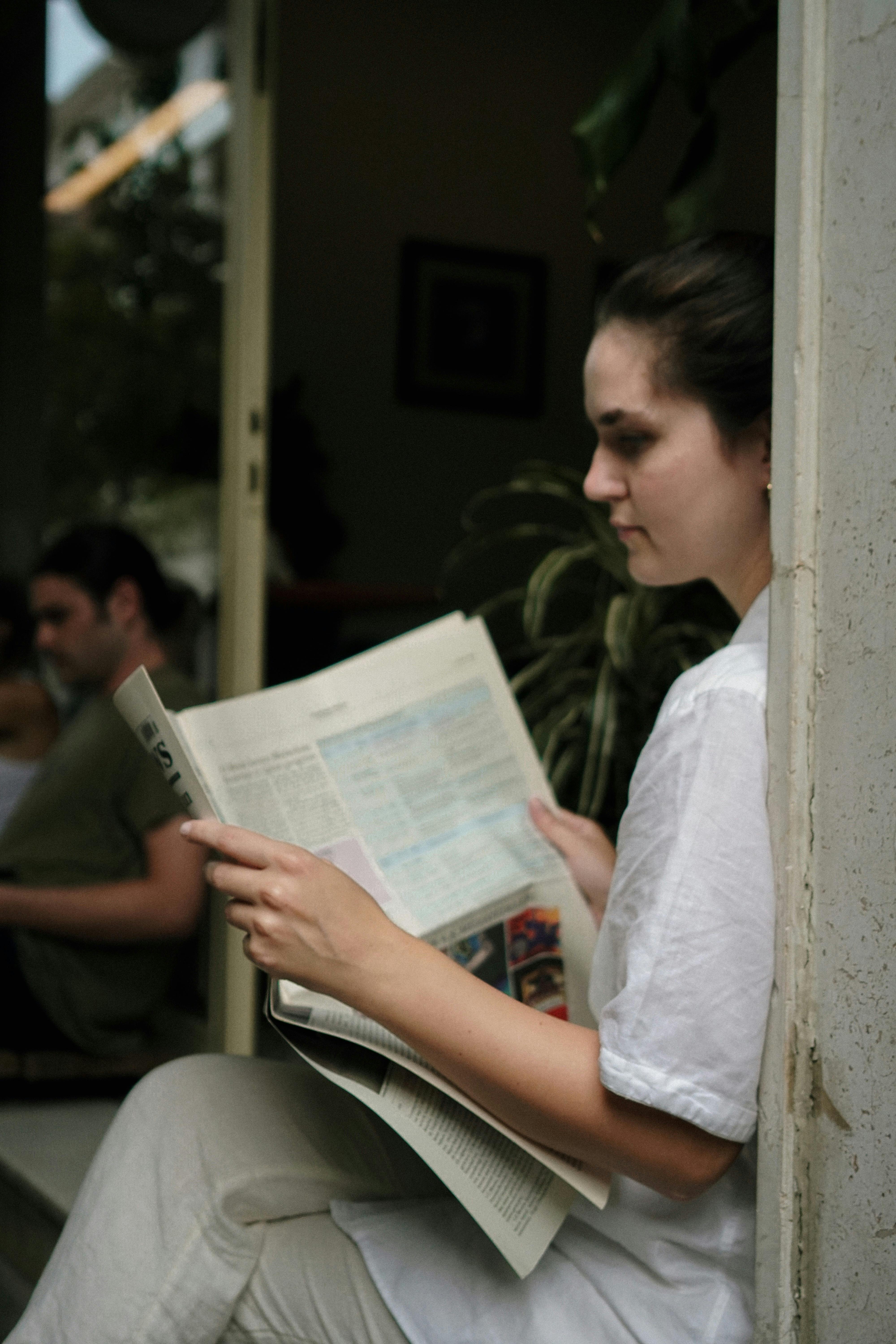 Young woman enjoying a quiet moment reading a newspaper indoors.