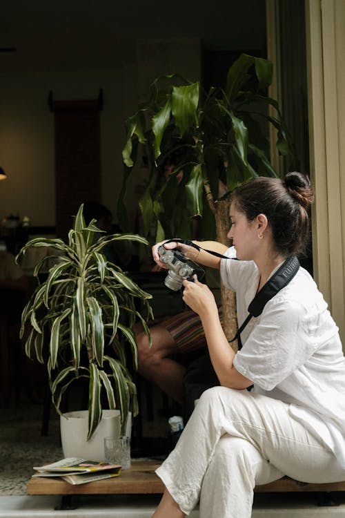 Woman in White Shirt Holding a Camera while Taking Photo of a Potted Plant