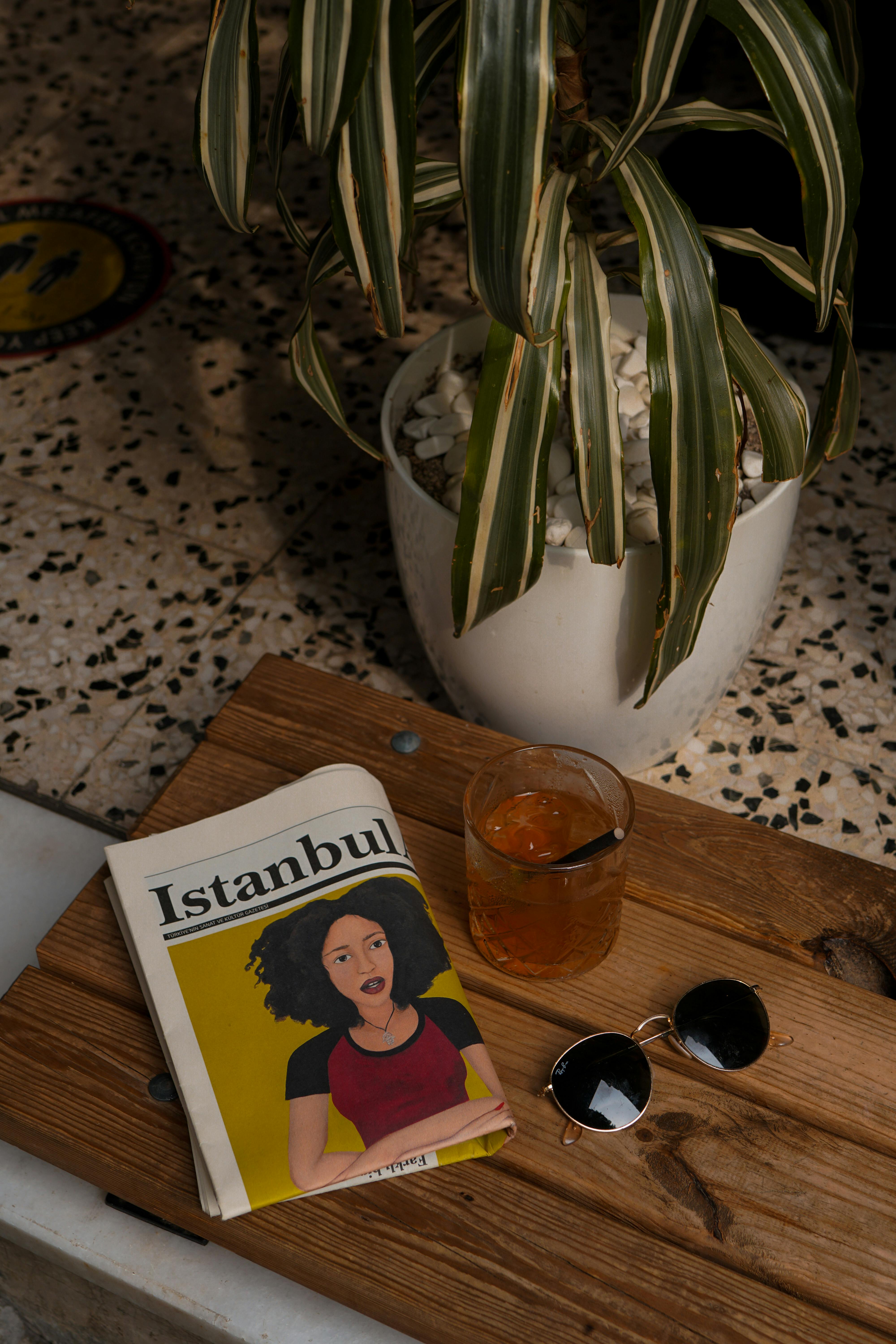 Elegant setup featuring a drink, magazine, and sunglasses on a wooden table.