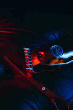 Close-up of hair clipper and scissors in artistic lighting, vibrant red and blue tones.