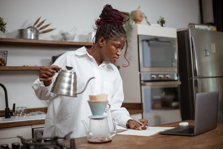 Woman Making Coffee And Looking At A Laptop Standing On A Kitchen Counter 