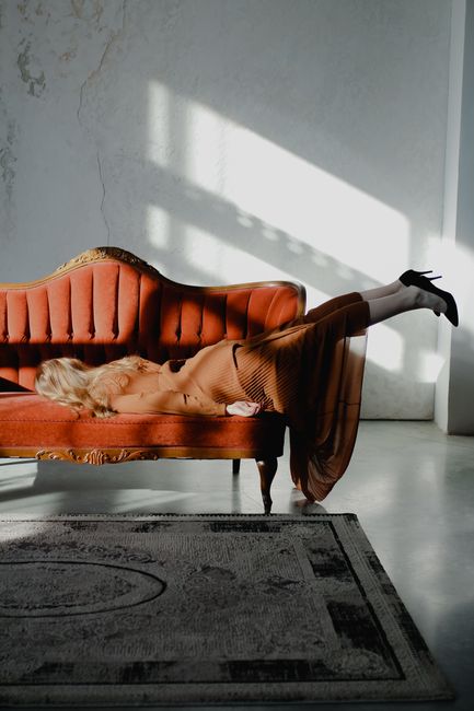 Photo of a stylish woman lying elegantly on a vintage sofa with sunlit background, offering a blend of fashion and relaxation.