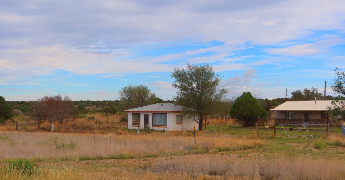Quaint rural houses surrounded by grass, under a cloudy summer sky.
