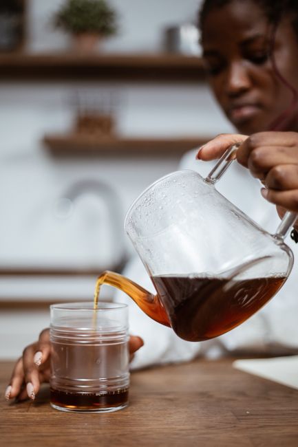 Close-up of a woman pouring freshly brewed coffee into a glass cup in a cozy kitchen setting.