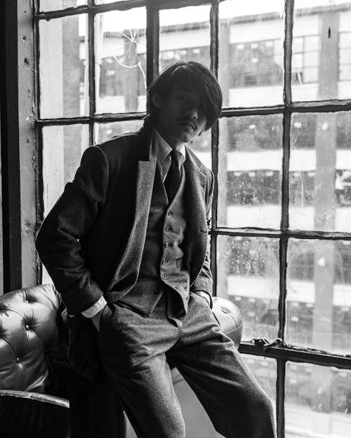 Grayscale Photo of a Man in a Suit Posing by the Window