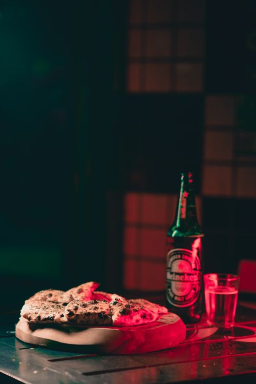 Free Heineken beer bottle and rustic pizza on a wooden board creating a cozy dining atmosphere. Stock Photo