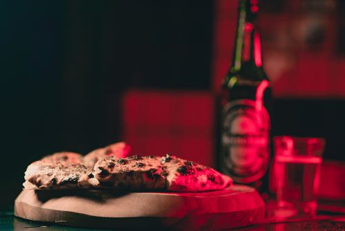 Free Artistic shot of bread on paper with a beer bottle in a dimly lit setting. Stock Photo