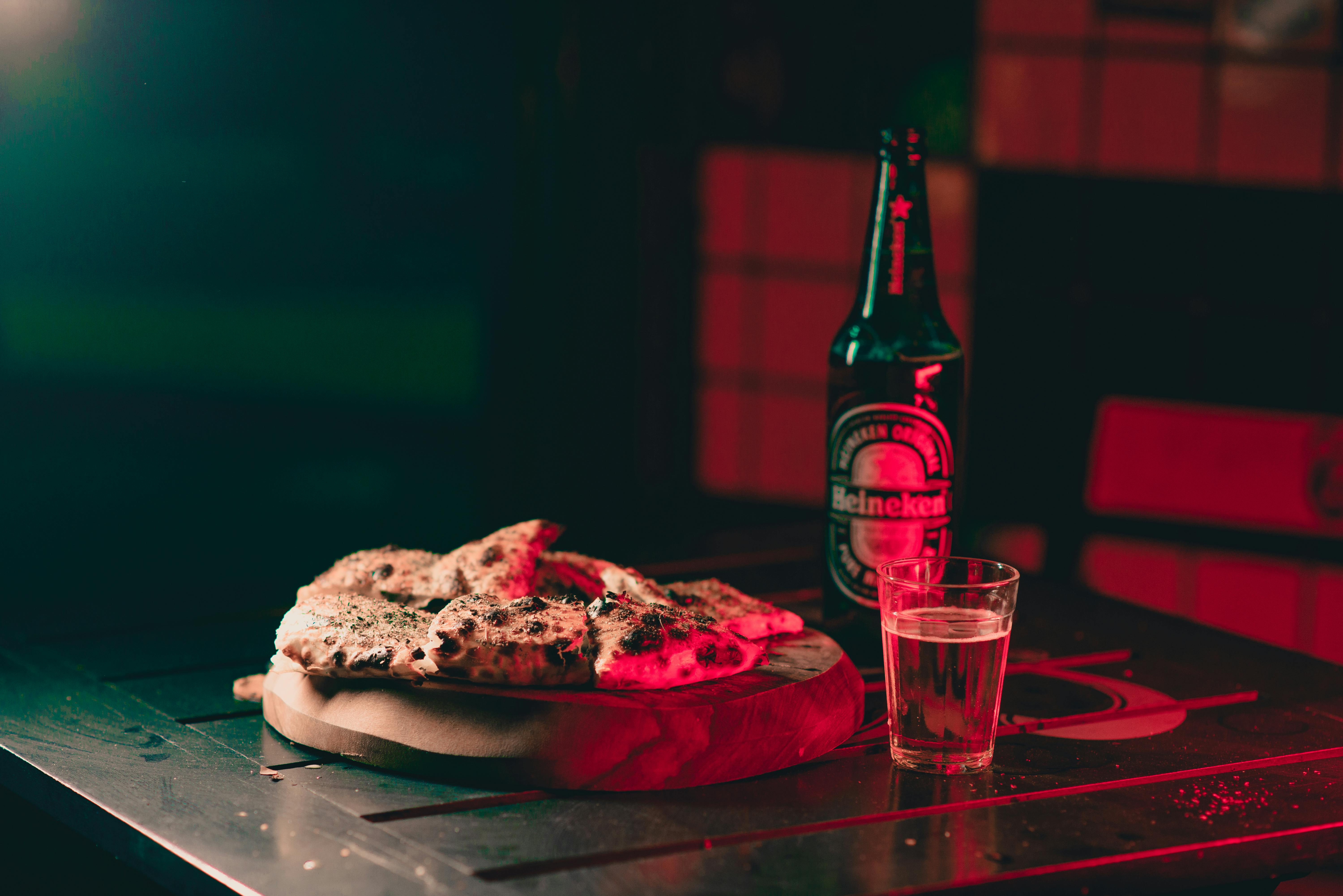 A cozy setting with pizza and Heineken beer bottle on a wooden board.