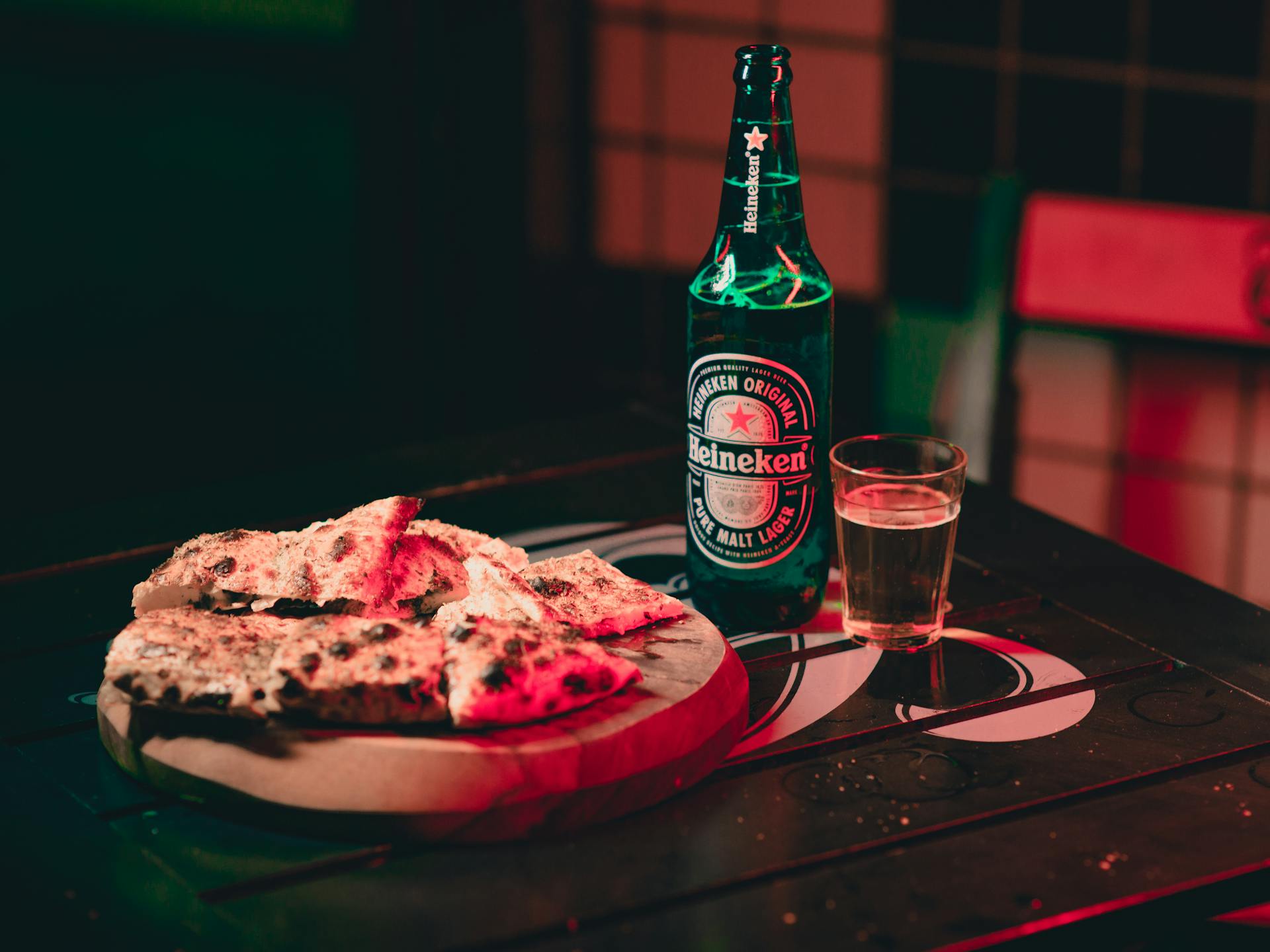 Cozy indoor setting with Heineken beer and pizza on a wooden table, perfect for casual dining.