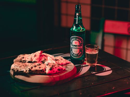 Free Cozy indoor setting with Heineken beer and pizza on a wooden table, perfect for casual dining. Stock Photo