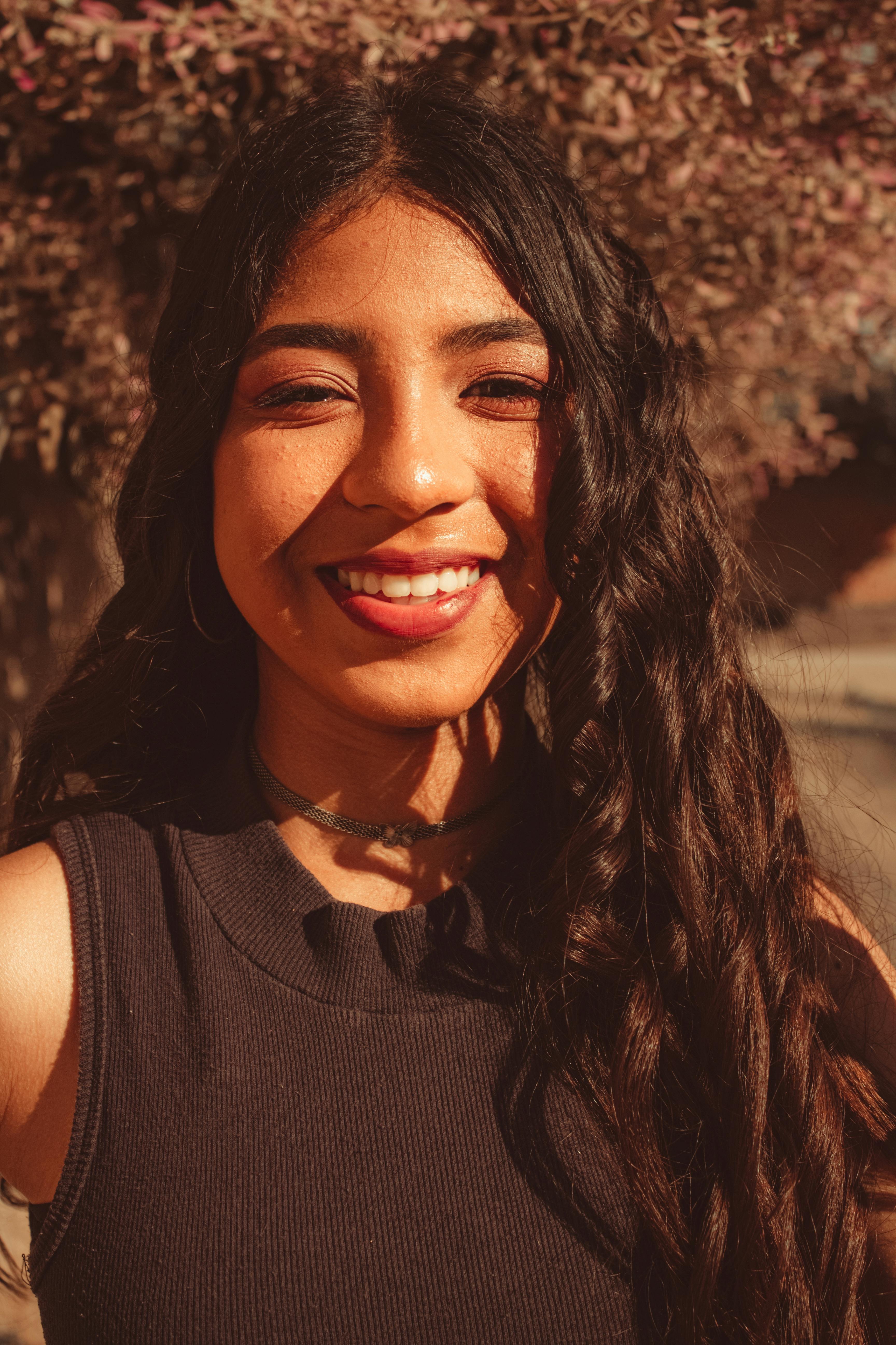 Portrait of a smiling woman with curly hair enjoying a sunny day outdoors.