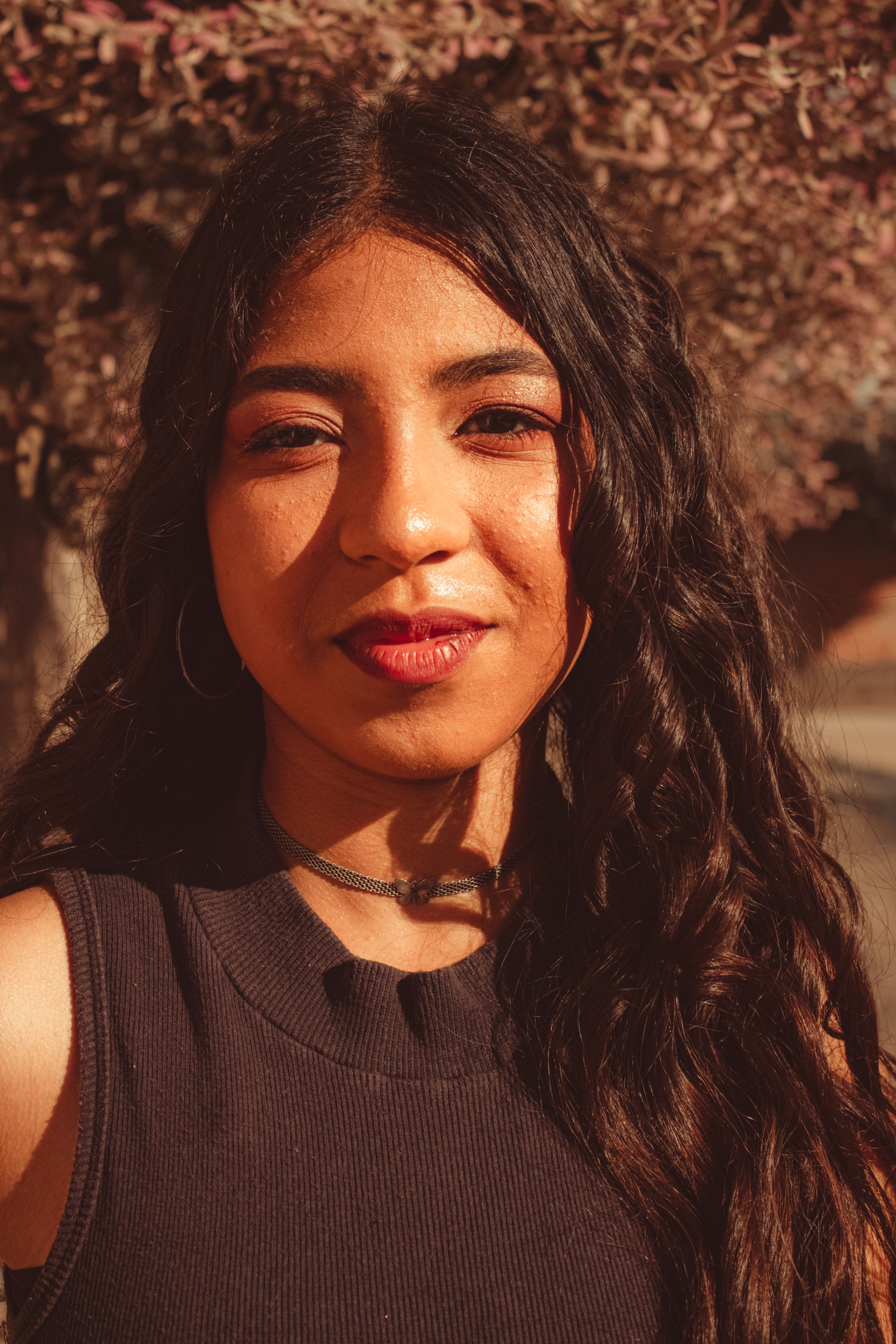 Close-up portrait of a young woman in a black tank top, captured in warm natural sunlight.