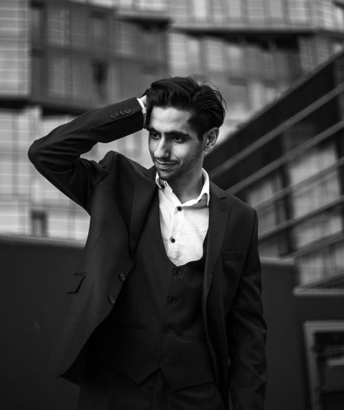 Free A confident man in a suit poses with hand on head against modern architecture. Stock Photo