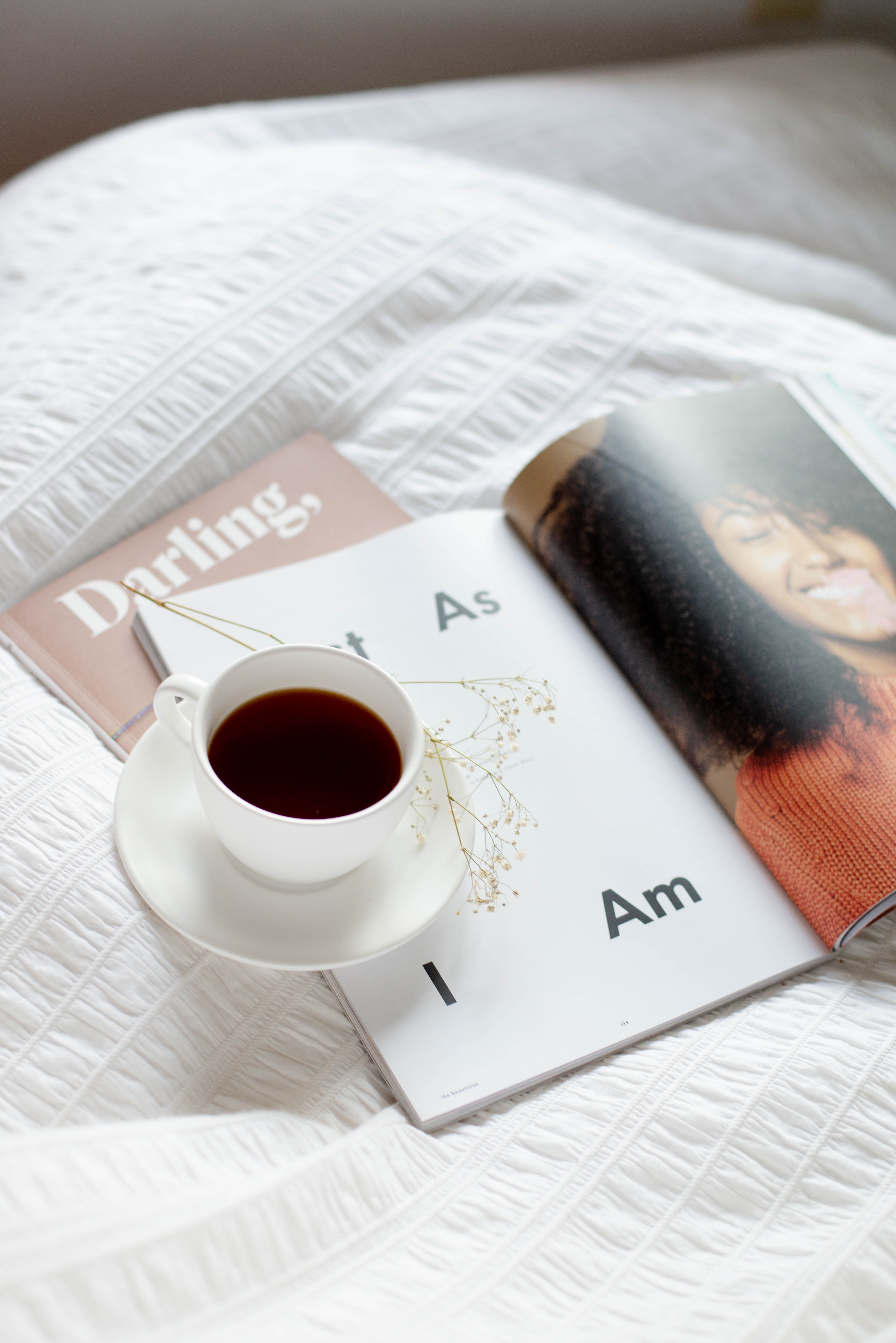 A white cup of tea on a bed with an open magazine in bright light. Cozy reading moment.