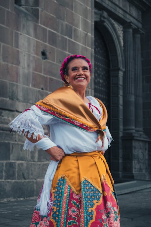 A Woman in Traditional Outfit Standing Near Brown Brick Building