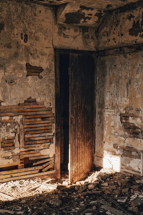 Free A decaying room with a partially open wooden door, revealing crumbling walls and debris. Stock Photo