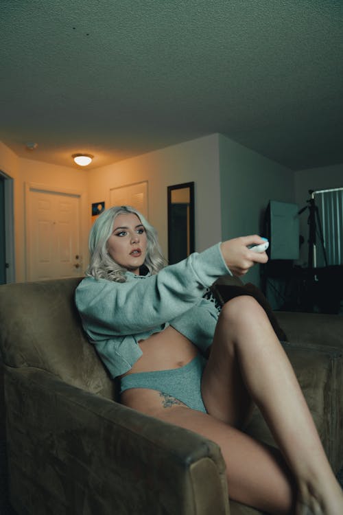 A Woman in Gray Sweatshirt and Panty Sitting on Chair Holding a Remote Control