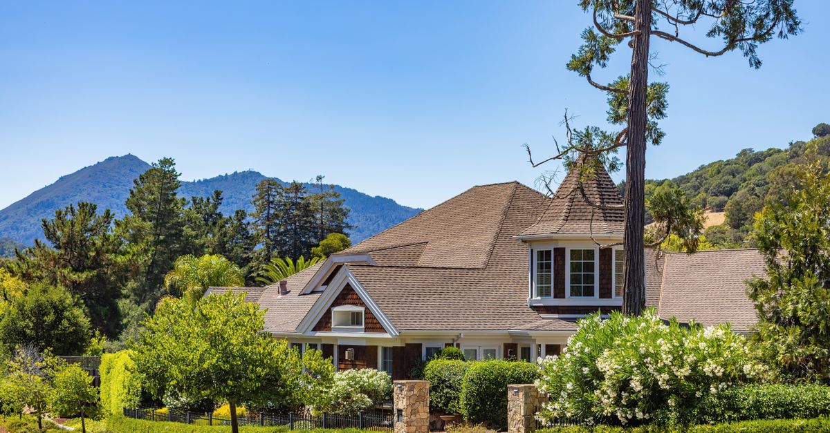 Charming house surrounded by lush greenery with scenic mountains in the background.