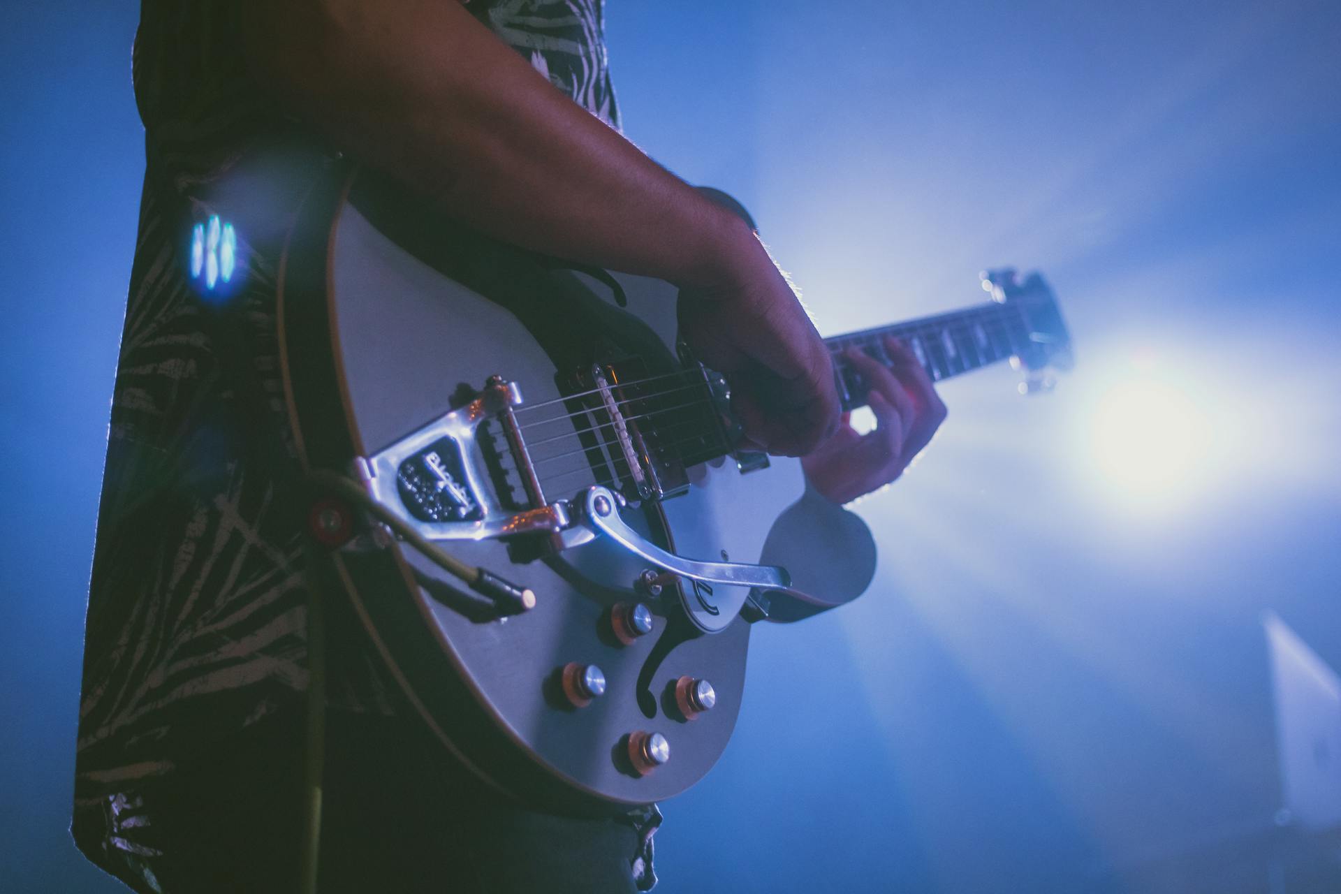 Close-up of a musician playing an electric guitar under stage lights during a live performance.