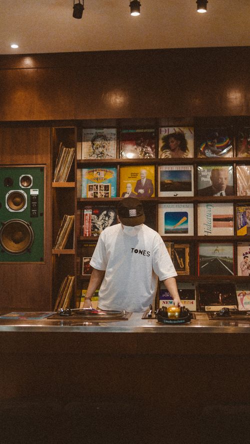 Free A DJ mixes vinyl records on a turntable in a cozy music store with wooden decor. Stock Photo