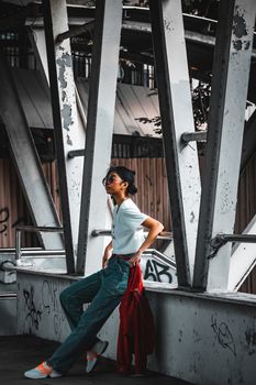 Fashionable woman in denim and sunglasses posing on a modern urban bridge.