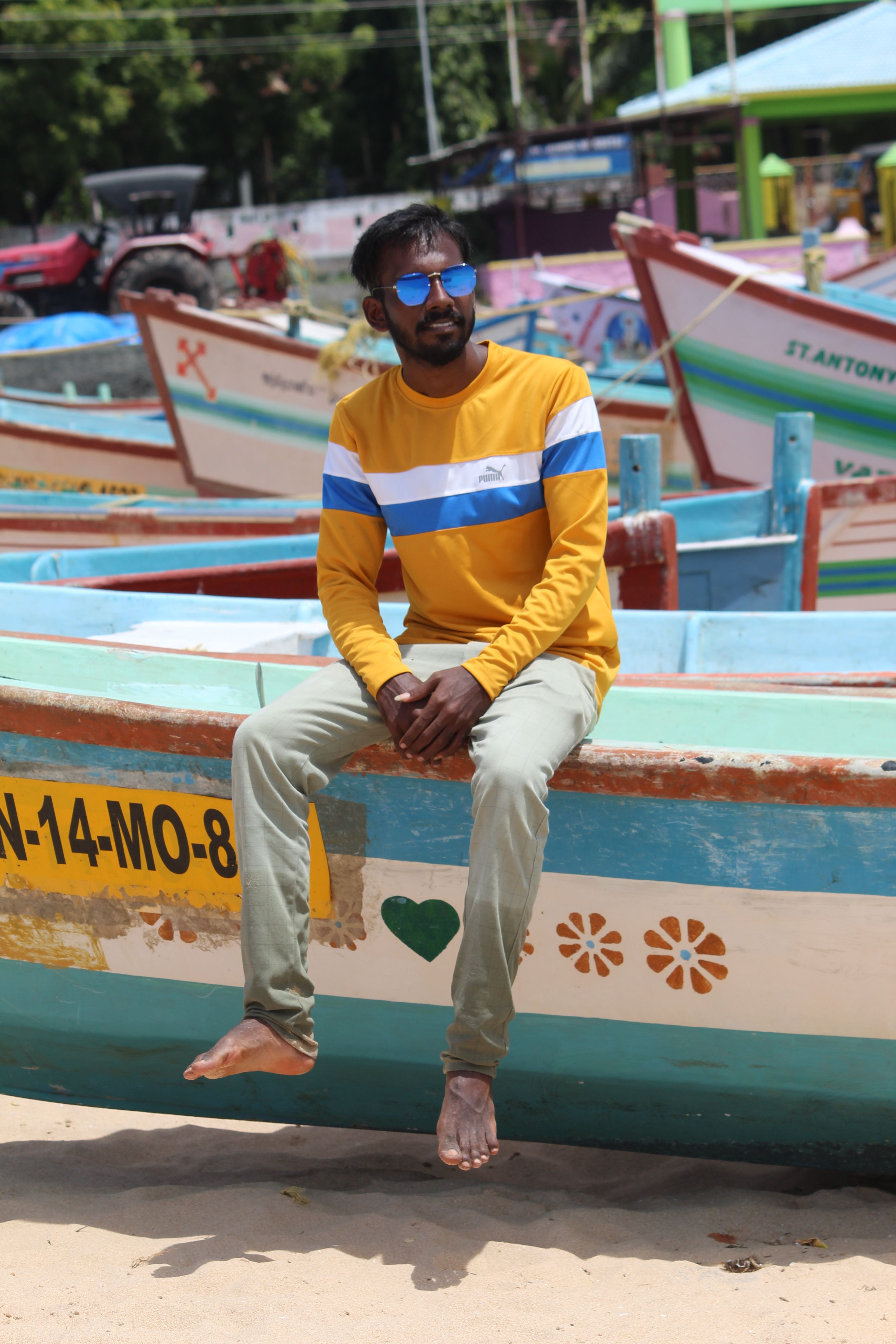 Man sitting on a vibrant boat in Kanyakumari's sandy beach under sunny skies.