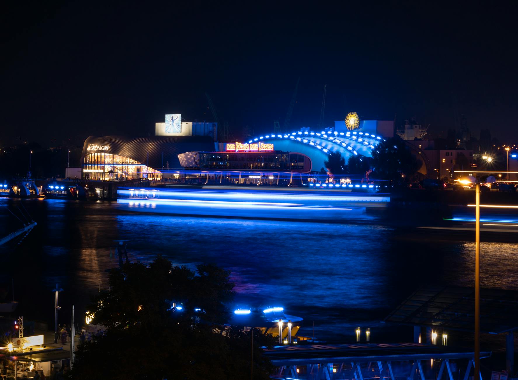 A vibrant night scene of Hamburg harbor with illuminated buildings and reflections on water.
