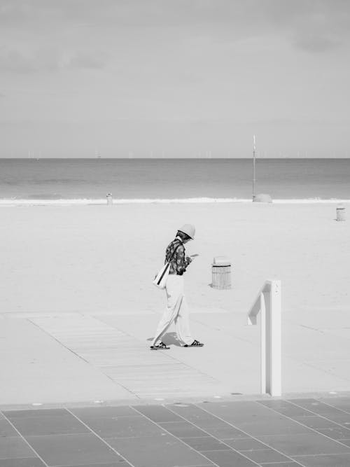 Grayscale Photo of a Person Walking on the Beach
