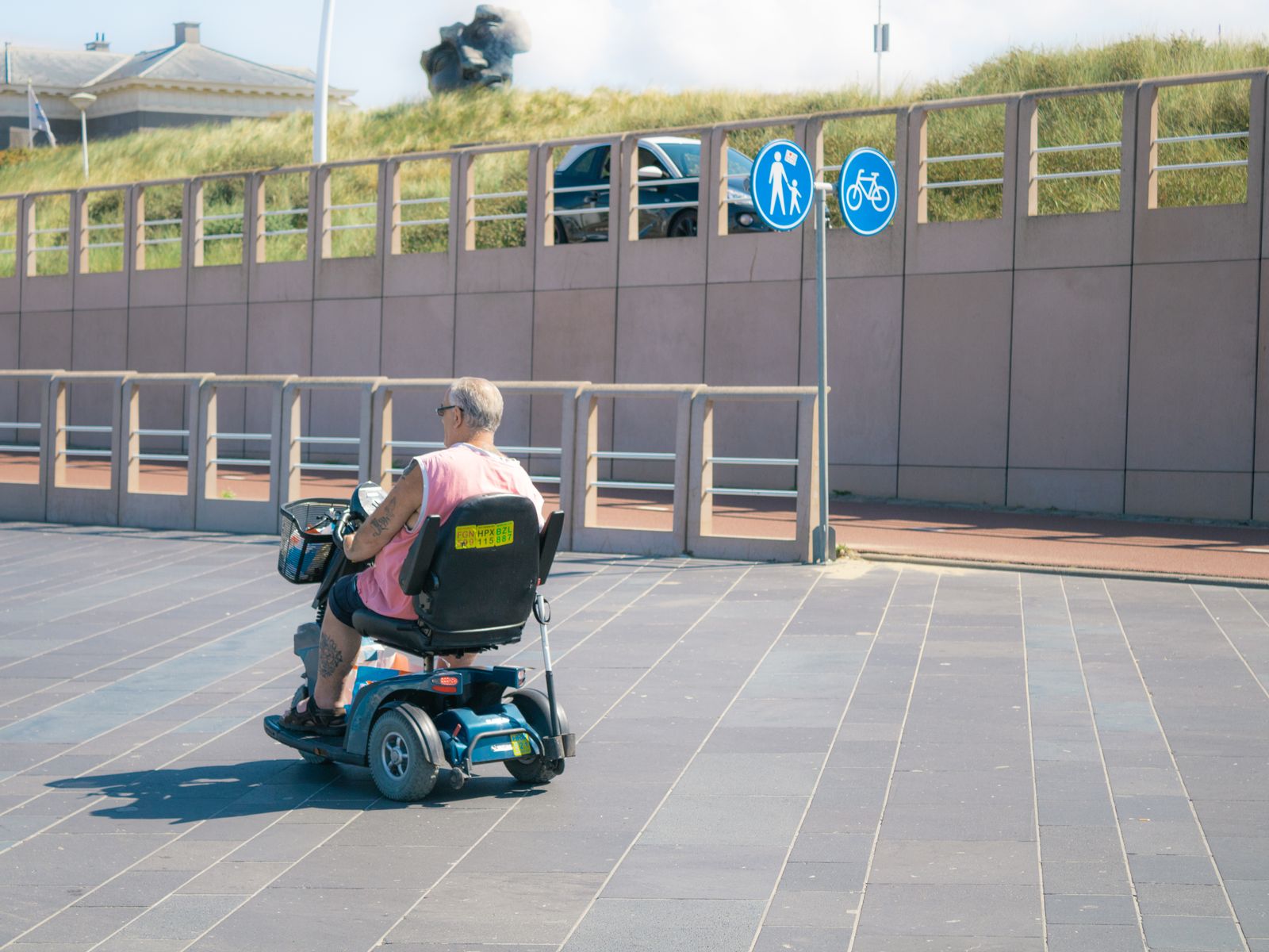 A senior man rides a three-wheel electric mobility scooter down a sunny street