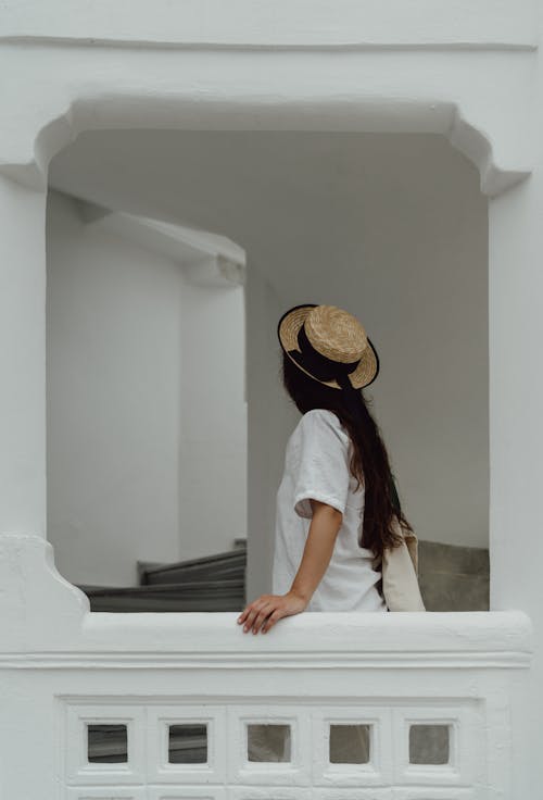 A Woman in White Shirt Wearing Sun Hat while Leaning on a Concrete Railing