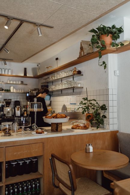 A warm café scene featuring a barista preparing treats with empty seating and rustic décor.