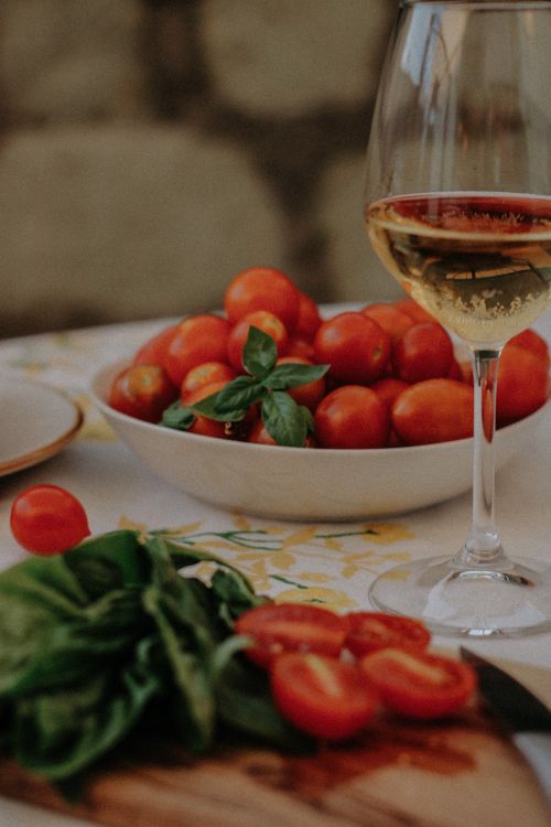 Free Bowl of cherry tomatoes with basil alongside a glass of white wine on a rustic table setting. Stock Photo