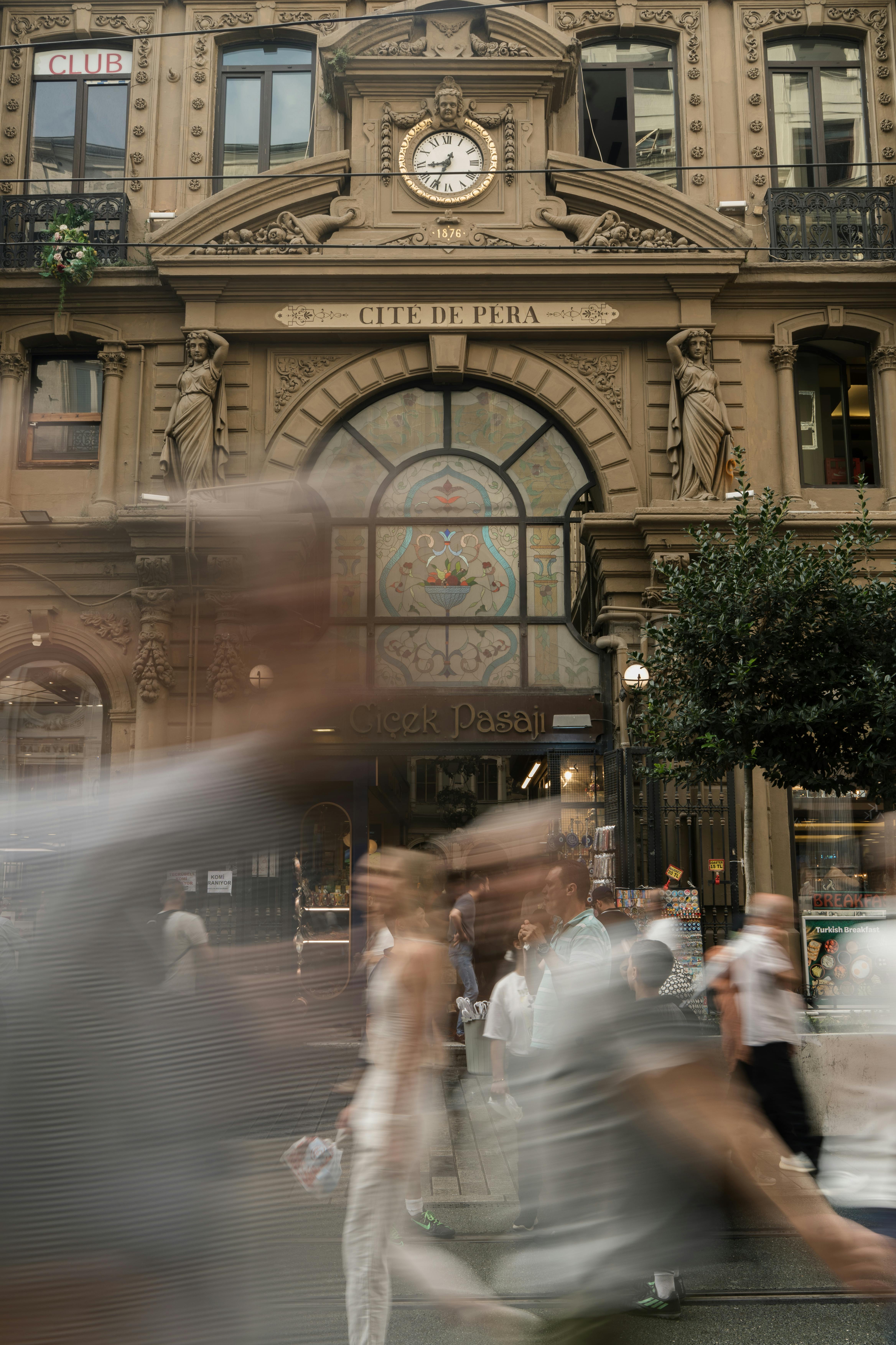 A busy street with people walking past a historic building, showcasing blurred motion and architectural detail.