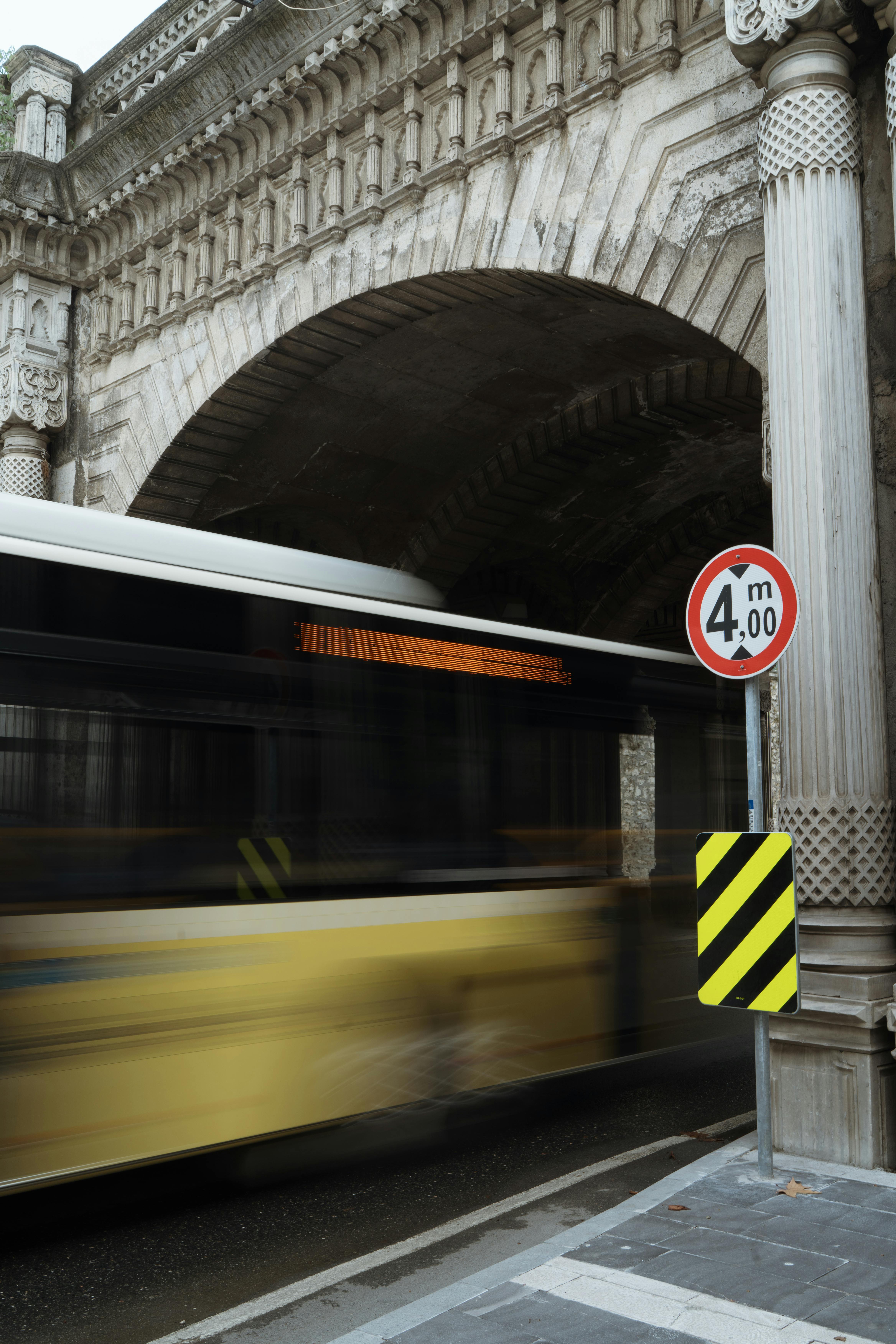 Yellow bus in motion under a historical stone archway, capturing transportation dynamics.