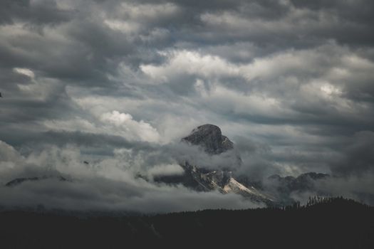 A striking view of a mountain peak surrounded by thick, dramatic clouds in an overcast sky.
