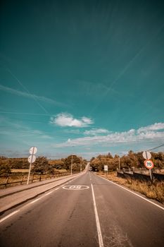 A scenic empty road stretching into the horizon beneath a clear blue sky with visible signages.