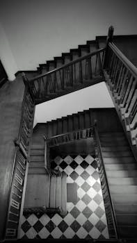 A black and white view of a wooden staircase with a checkered floor pattern, creating a classic architectural look.