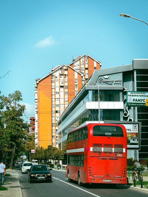 Free Vibrant cityscape featuring a red double-decker bus on a Skopje street with buildings and blue sky. Stock Photo