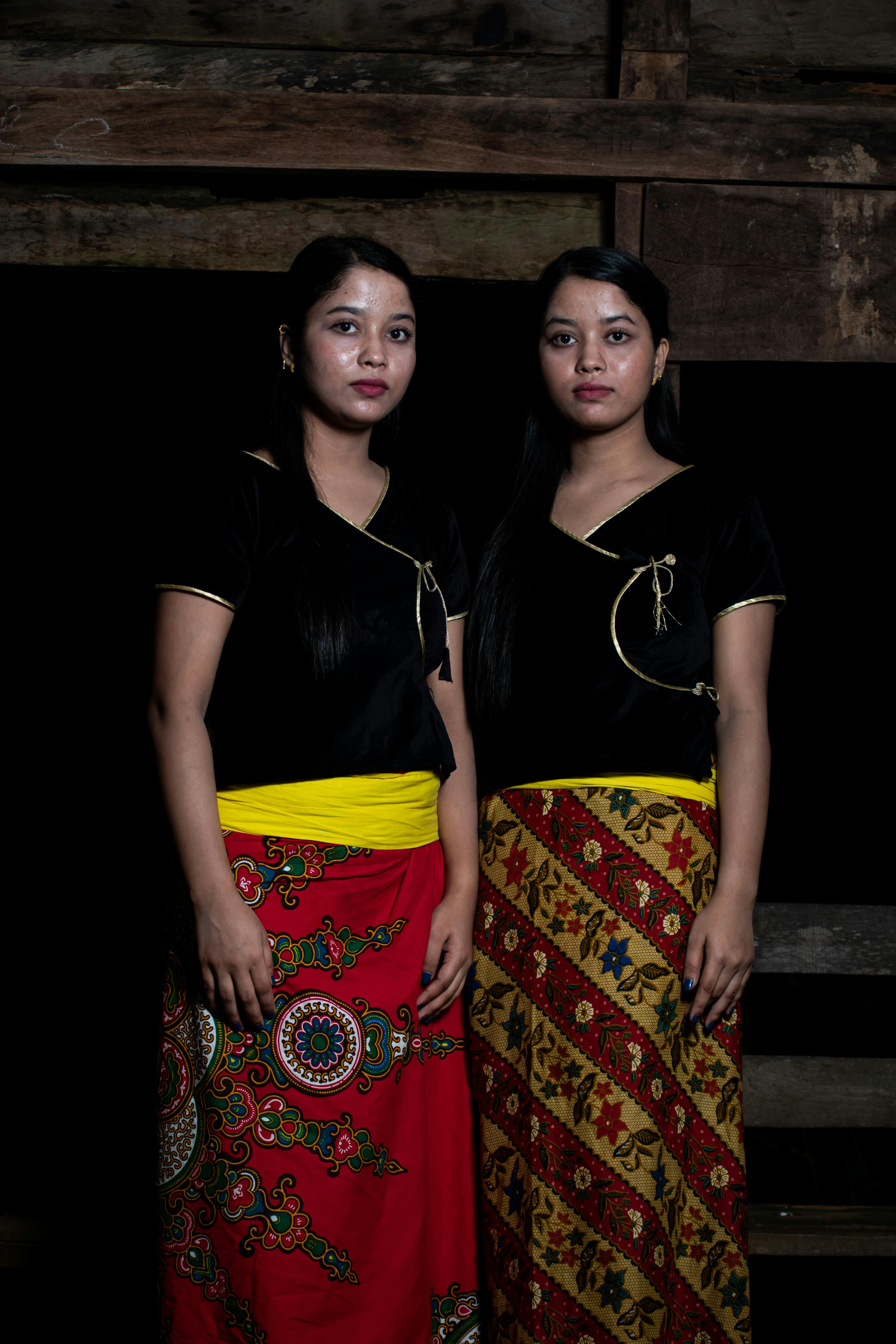 Two women posing in colorful traditional attire against a dark backdrop.